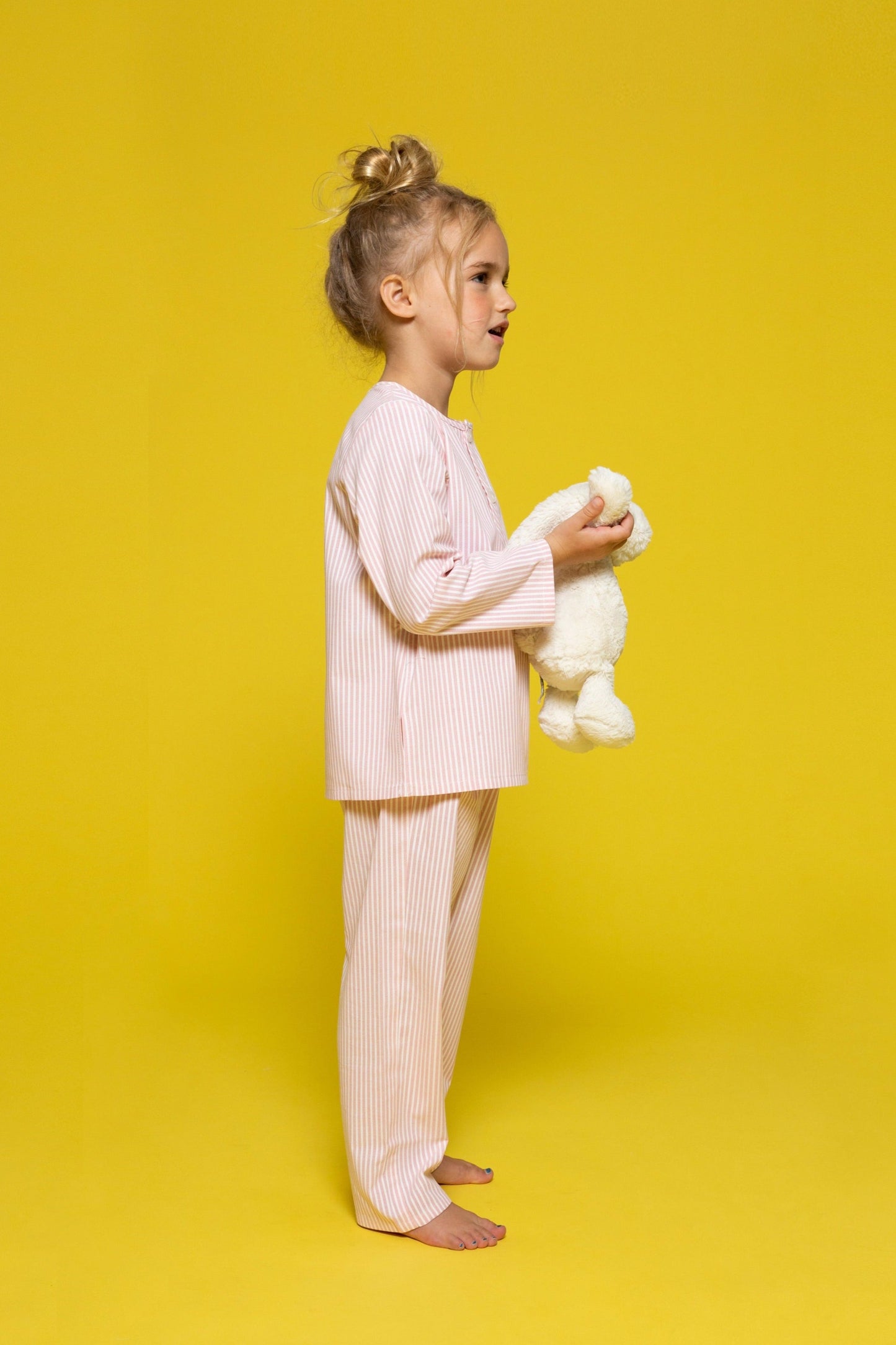 model wearing pink and white pinstripe pajamas and holding jellycat doll, good morning monsters woven pajamas, loungewear, sleepwear, loose-fitting pajamas, boys, girls, baby, unisex