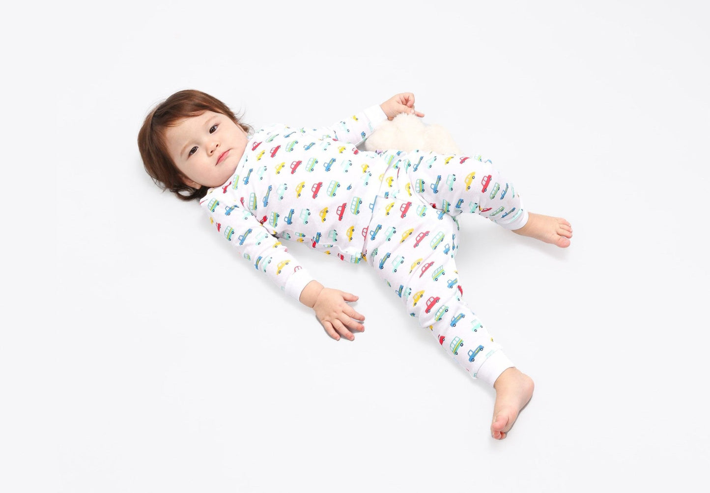 Toddler in long-sleeved, 100% GOTS certified organic cotton pajamas. 
 Pajamas are white, lightweight fabric with a vibrant, colorful, vehicles print with cars, jeeps, trucks, and buses.
good morning monsters pajamas, loungewear, sleepwear, pajamas, boys, girls, baby, unisex