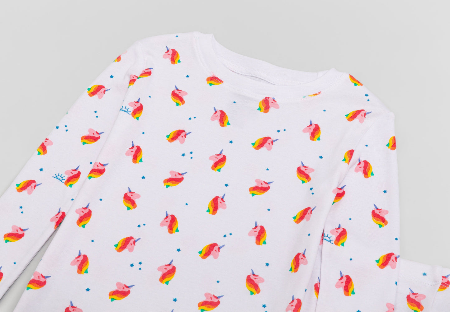 View of Pajama Set - Close up of unicorn print (with colorful unicorns, blue stars, and blue GMM logos). 
 Pajamas are white fabric with a vibrant unicorn print.  Pajamas are long-sleeved and made from GOTS certified, 100% organic cotton.
good morning monsters pajamas, loungewear, sleepwear, pajamas, boys, girls, baby, unisex