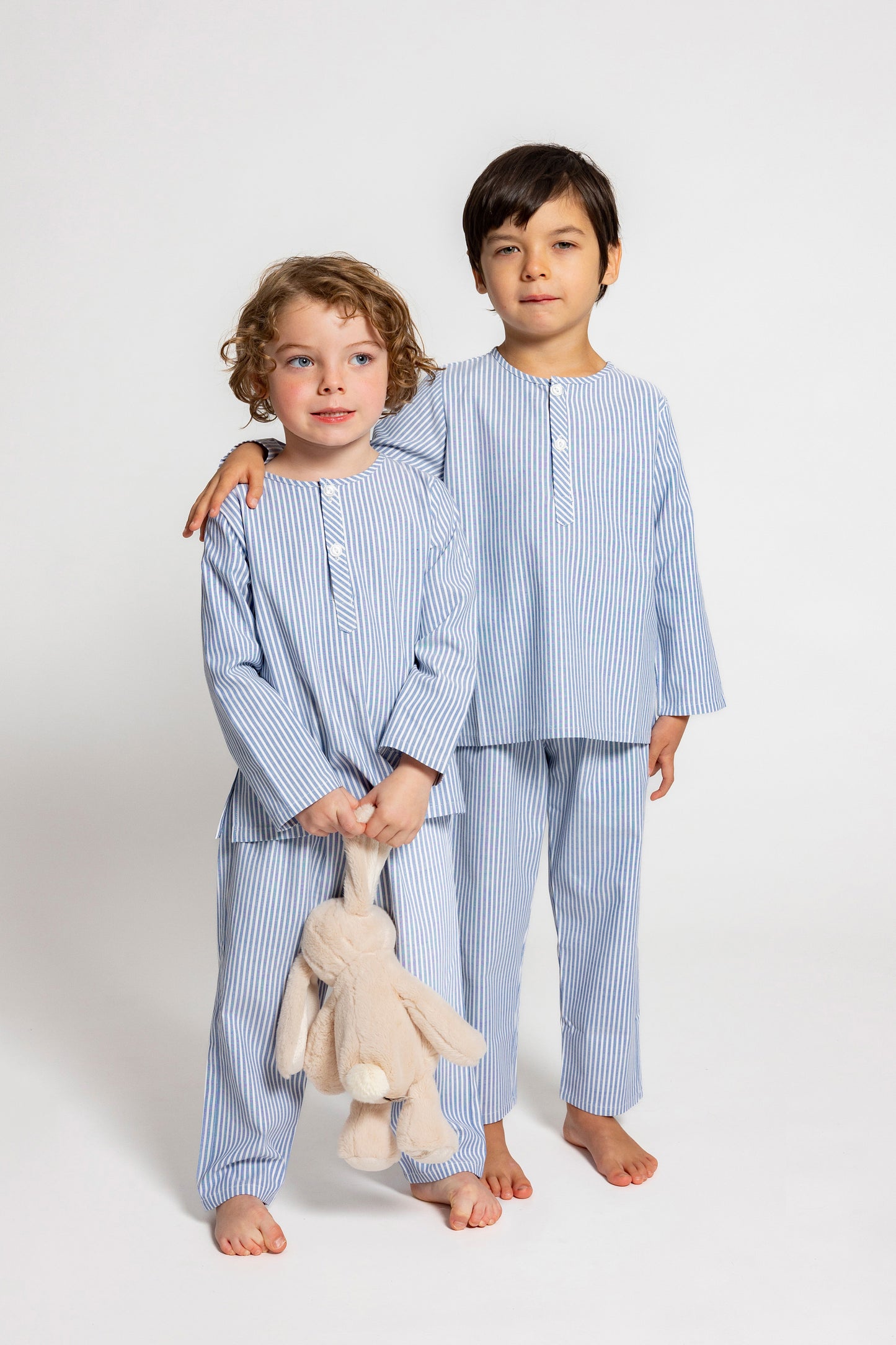 two models wearing blue and white pinstripe pajamas (one model is holding jellycat doll), good morning monsters woven pajamas, loungewear, sleepwear, loose-fitting pajamas, boys, girls, baby, unisex