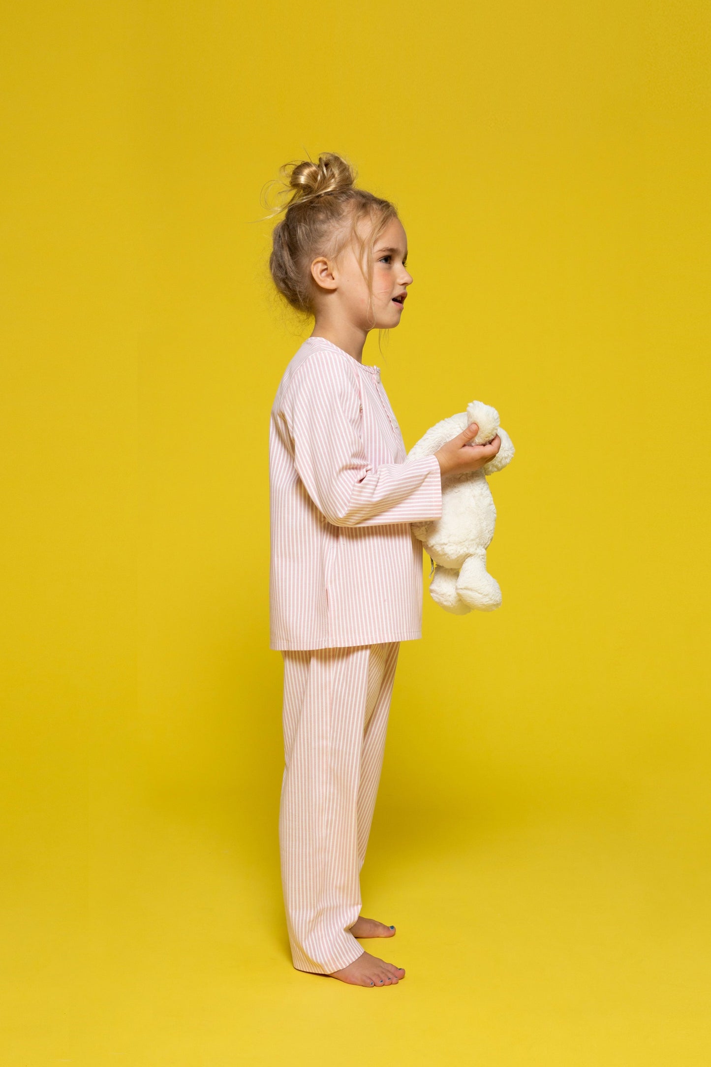 model wearing pink and white pinstripe pajamas and holding jellycat doll, good morning monsters woven pajamas, loungewear, sleepwear, loose-fitting pajamas, boys, girls, baby, unisex