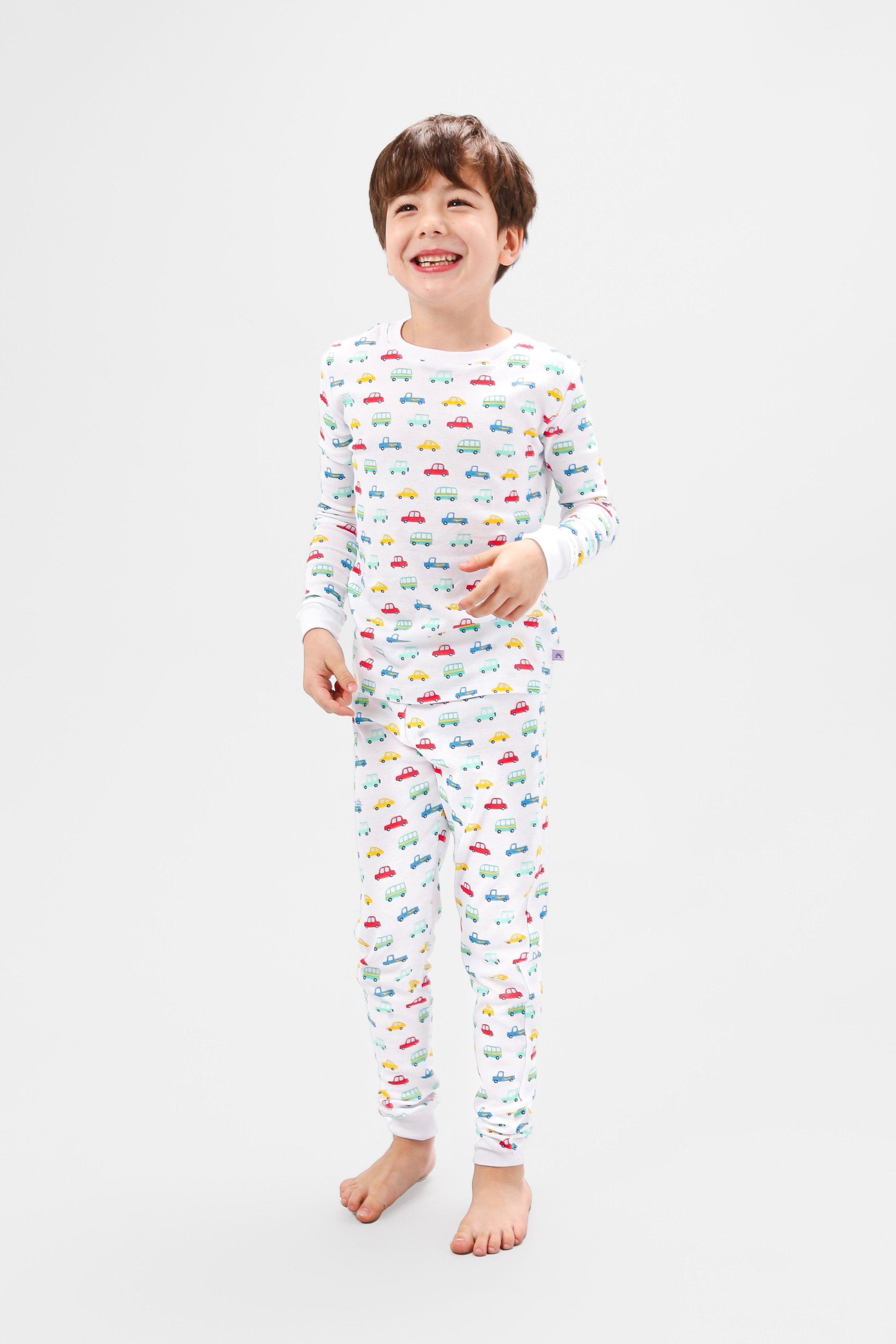 Front view of model wearing vehicles pajama set.  
Pajamas are white, lightweight fabric with a vibrant, colorful vehicles print with cars, jeeps, trucks, and buses.  Pajamas are long-sleeved and made from 100% GOTS certified organic cotton.
good morning monsters pajamas, loungewear, sleepwear, pajamas, boys, girls, baby, unisex