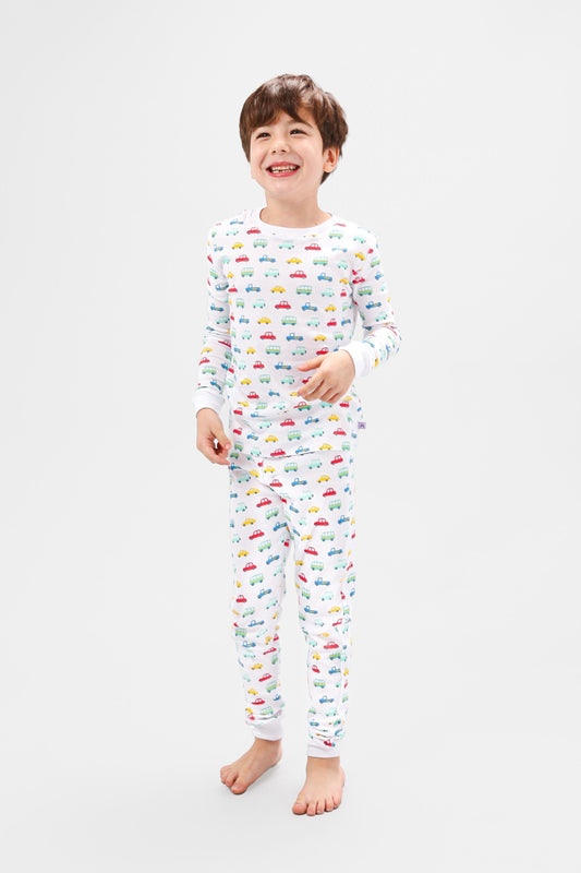 Front view of model wearing vehicles pajama set.  
Pajamas are white, lightweight fabric with a vibrant, colorful vehicles print with cars, jeeps, trucks, and buses.  Pajamas are long-sleeved and made from 100% GOTS certified organic cotton.
good morning monsters pajamas, loungewear, sleepwear, pajamas, boys, girls, baby, unisex