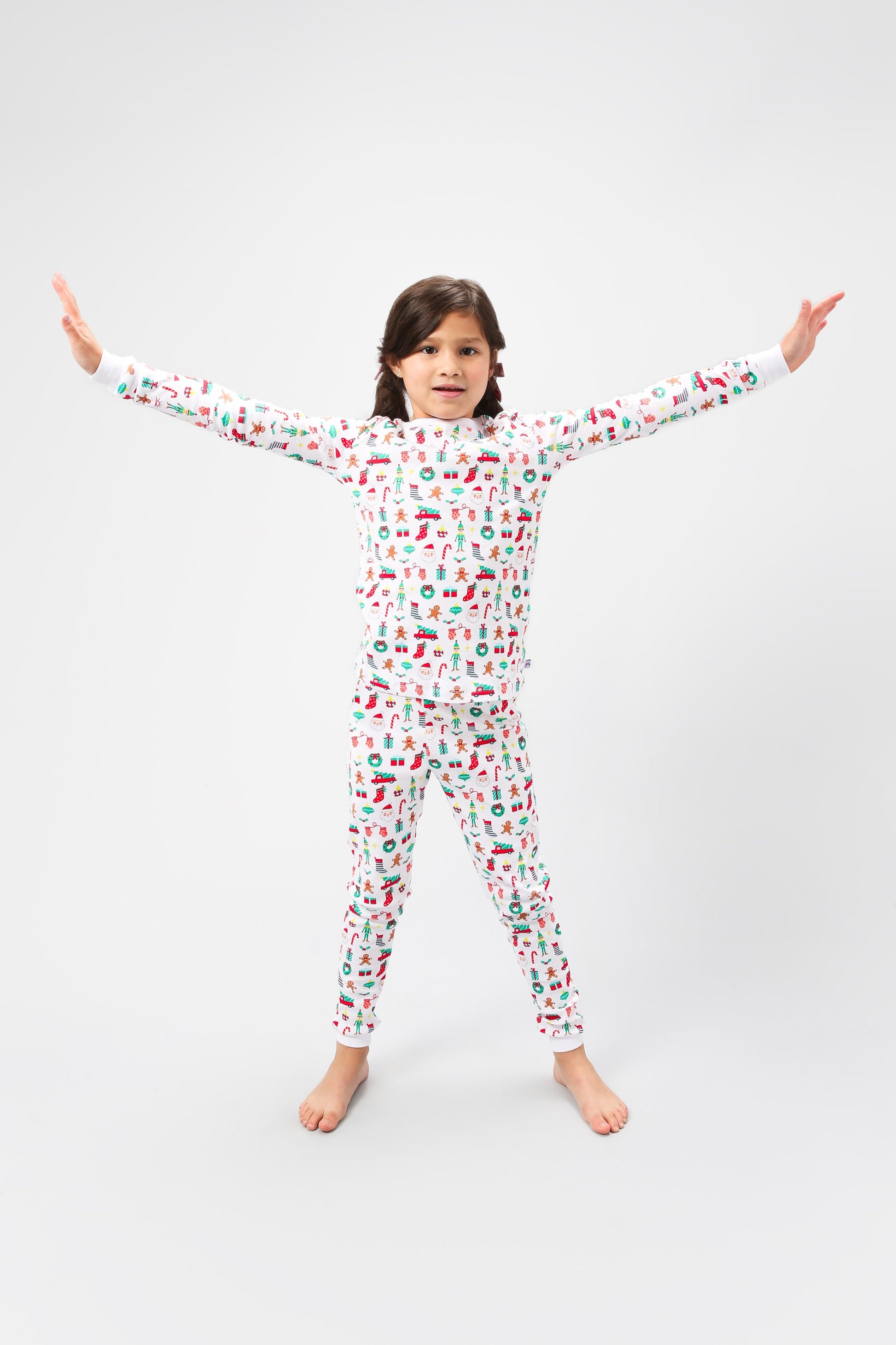 Front view of model arms out posing, wearing Christmas, festive, Santa, Elves, Classic Christmas, Holiday, Ornaments, Stockings, Gingerbread, Red Trucks pajama set.  
Pajamas are white, lightweight fabric with a vibrant Christmas print.   Pajamas are long-sleeved and made from GOTS certified, 100% organic cotton.
good morning monsters pajamas, loungewear, sleepwear, pajamas, boys, girls, baby, unisex