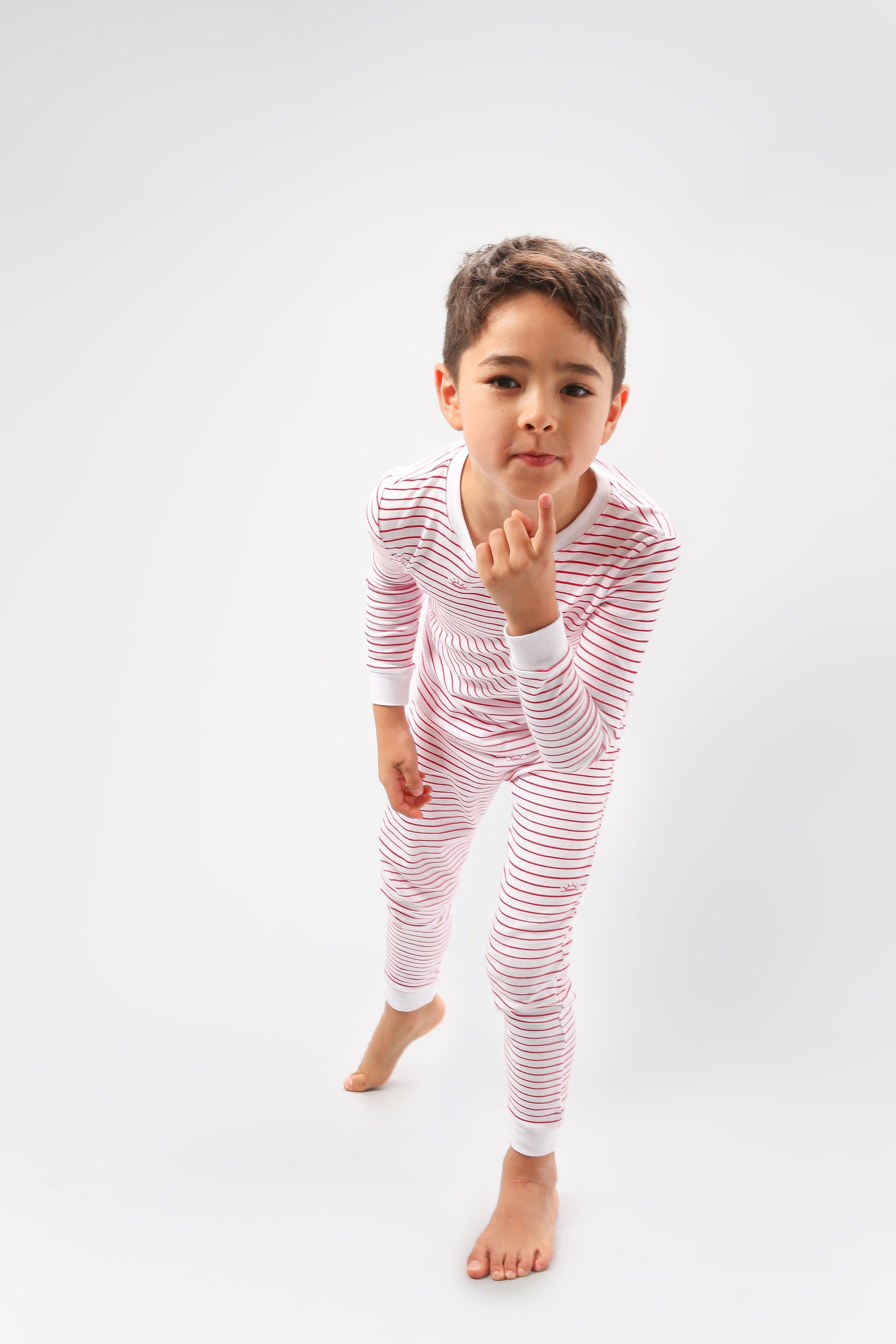 Model posing wearing red stripes pajama set.  
Pajamas are white, lightweight  fabric with playful red stripes throughout (along with our GMM logo sprinkled in).  Pajamas are long-sleeved and made from GOTS certified, 100% organic cotton.
good morning monsters pajamas, loungewear, sleepwear, pajamas, boys, girls, baby, unisex