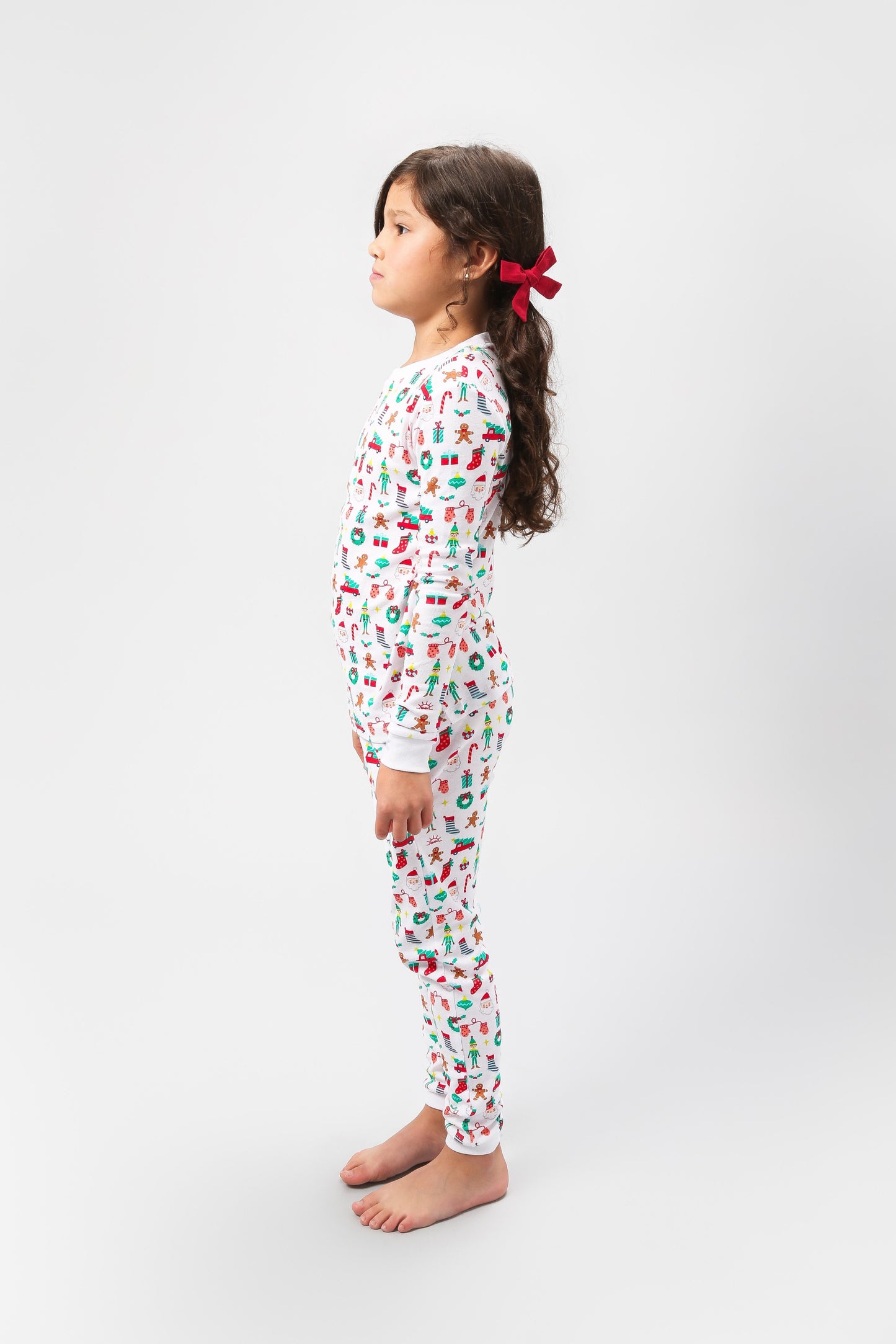 Side view of model wearing Christmas, festive, Santa, Elves, Classic Christmas, Holiday Ornaments, Stockings, Gingerbread, Red Trucks pajama set.  
Pajamas are white, lightweight fabric with a vibrant Christmas print.  Pajamas are long-sleeved and made from GOTS certified, 100% organic cotton.
good morning monsters pajamas, loungewear, sleepwear, pajamas, boys, girls, baby, unisex